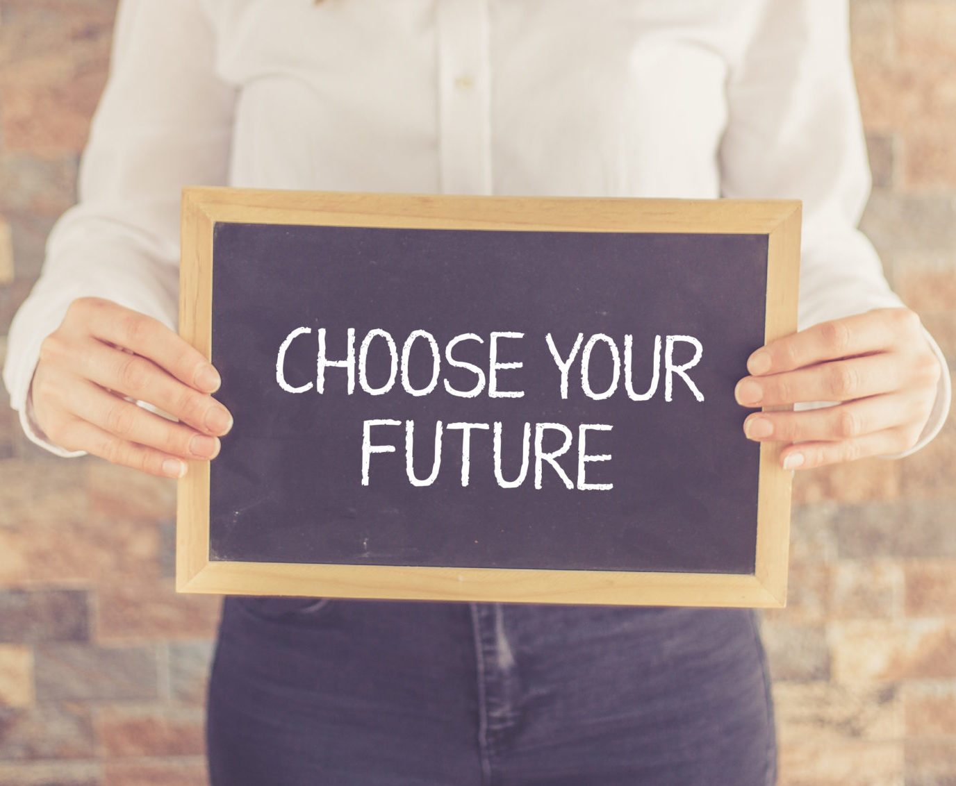 a person wearing a white shirt and dark pants holding a blackboard with the words "choose your future" written on them in front of a brick wall